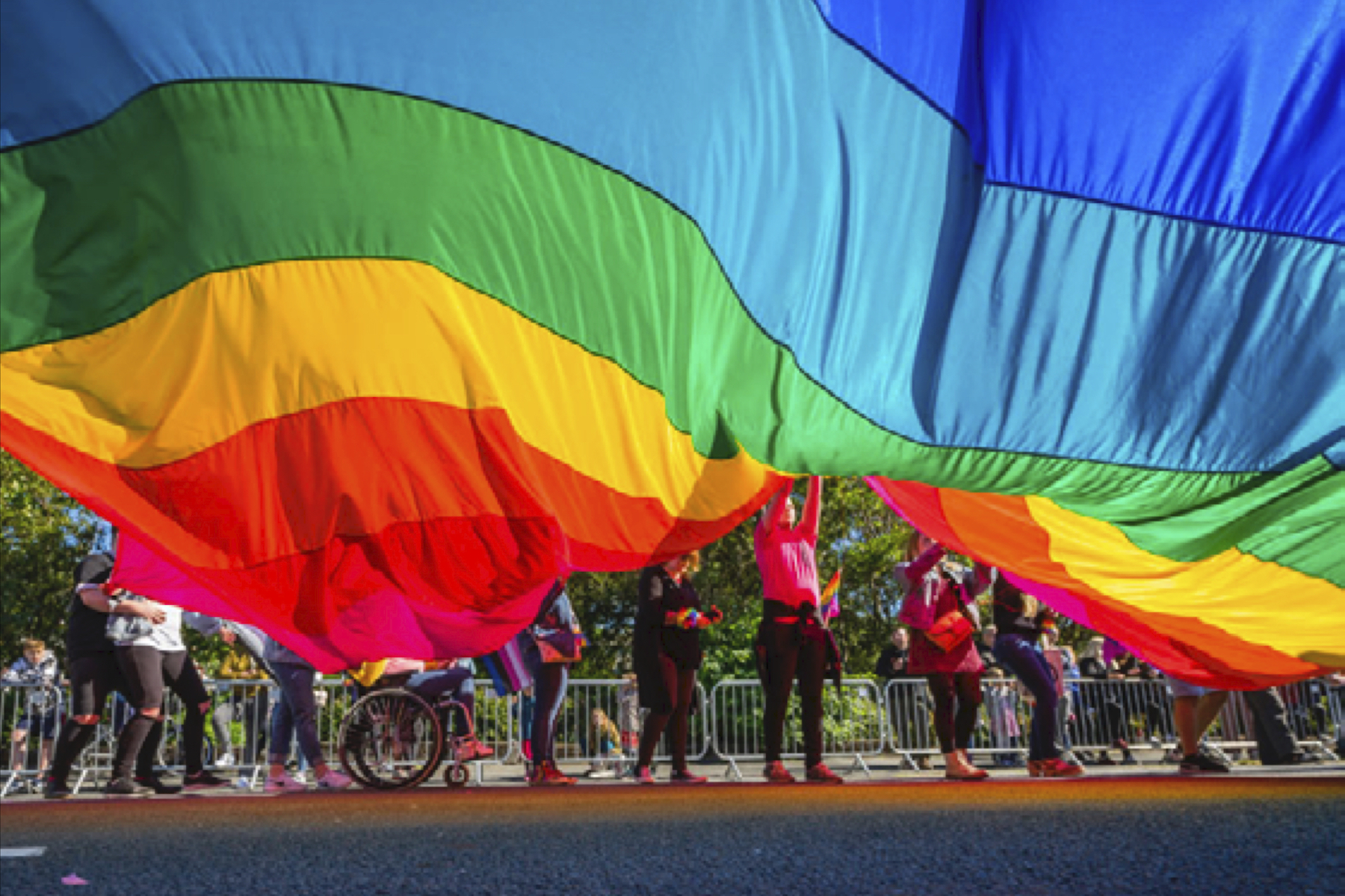 Line of people partially visible under a giant rainbow flag